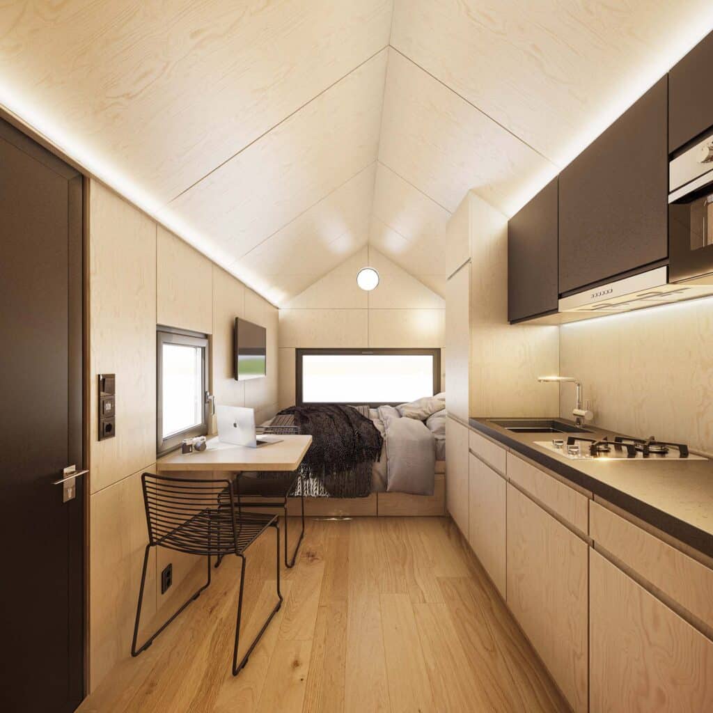 Intérieur moderne d'une tiny house avec un design en bois clair, comprenant un espace de bureau, une cuisine compacte et un lit.